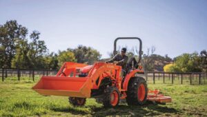 Person driving a Kubota L-Series tractor with attachment in a field.