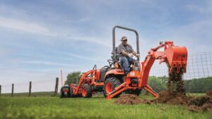 Person in a Kubota tractor with excavator attachments out in a field.