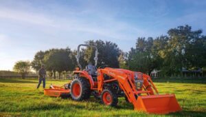Kubota L-Series Tractor on a field at sunset with a person walking behind it.