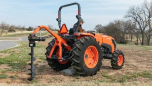 Land Pride HD25 Series Post Hole Digger mounted to the back of a Kubota tractor in a field next to a road.