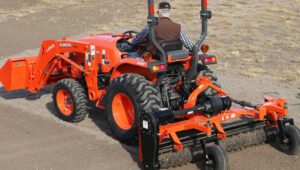 Tractor with a Land Pride PR16 Powered Rake mounted on the back.