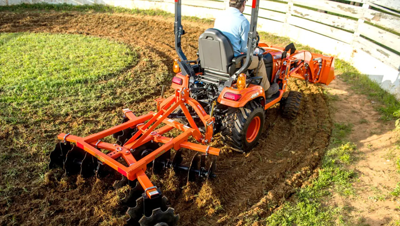 Person driving a Kubota tractor with a Land Pride DH15 Series Disc Harrows attachment in a horse pasture.