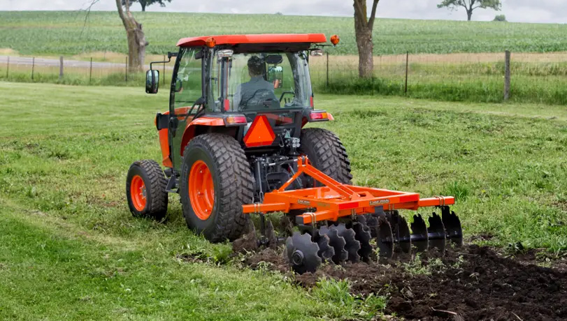 Person driving a tractor with a Land Pride DH25 Series Disc Harrows working a field with a fence in the background.
