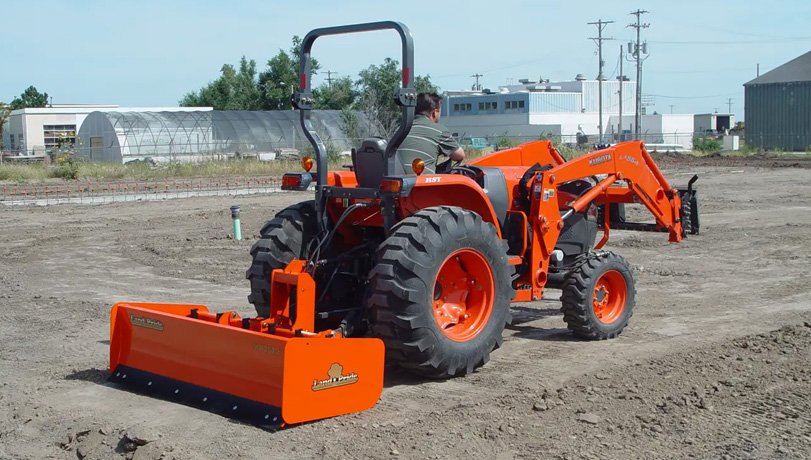 A person driving a tractor with a Land Pride HR25 Series Box Scraper attachment leveling cleared land for construction.