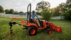 Land Pride PD10 Series Post Hole Digger mounted on a Kubota tractor near some trees and a pasture.