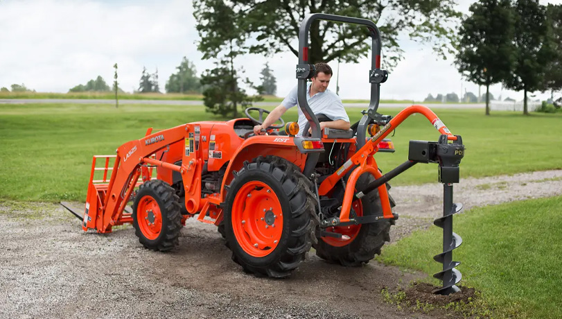 Land Pride PD15 Series Post Hole Digger mounted on a Kubota tractor on a piece of land near a river.
