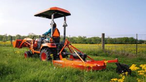 Person driving a Kubota tractor with a Land Pride RCR12 Series Rotary Cutter attachment on the back.