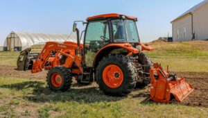 Land Pride Series RTA35 Rotary Tiller attachments attached to the back of a Kubota tractor near some agricultural buildings.