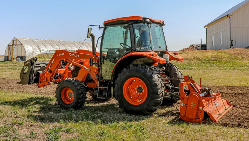Land Pride Series RTA35 Rotary Tiller attachments attached to the back of a Kubota tractor near some agricultural buildings.