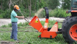 Worker using a Land Pride WC1504 Wood Chipper attached to a Kubota tractor grinding down a tree branch.