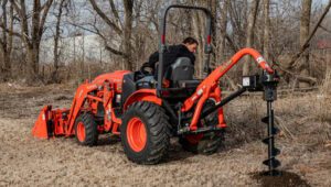Land Pride PD25 Series Post Hole Digger mounted on a Kubota tractor near some trees.