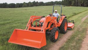 Person driving a Kubota tractor on a dirt path with a rotary cutter attachment on the back.