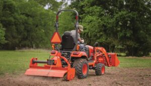 Person driving a Kubota tractor with a box blade attachment on the back.