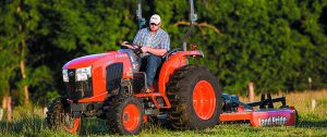 Person driving a Kubota L-Series tractor with a Land Pride attachment on the back.