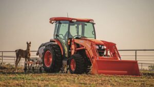 Kubota MX Series tractor with an excavator attachment on the front in a horse pasture.