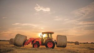 Kubota tractor in a livestock pasture at sunset with hay spear attachments.