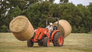 Person driving a Kubota tractor in a field with hay spear attachment.