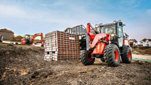 Person on a construction site driving a Kubota R640 Wheel Loader carrying a stack of bricks.
