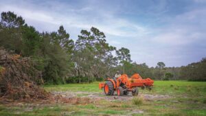 Person clearing land using a Kubota L-Series tractor.