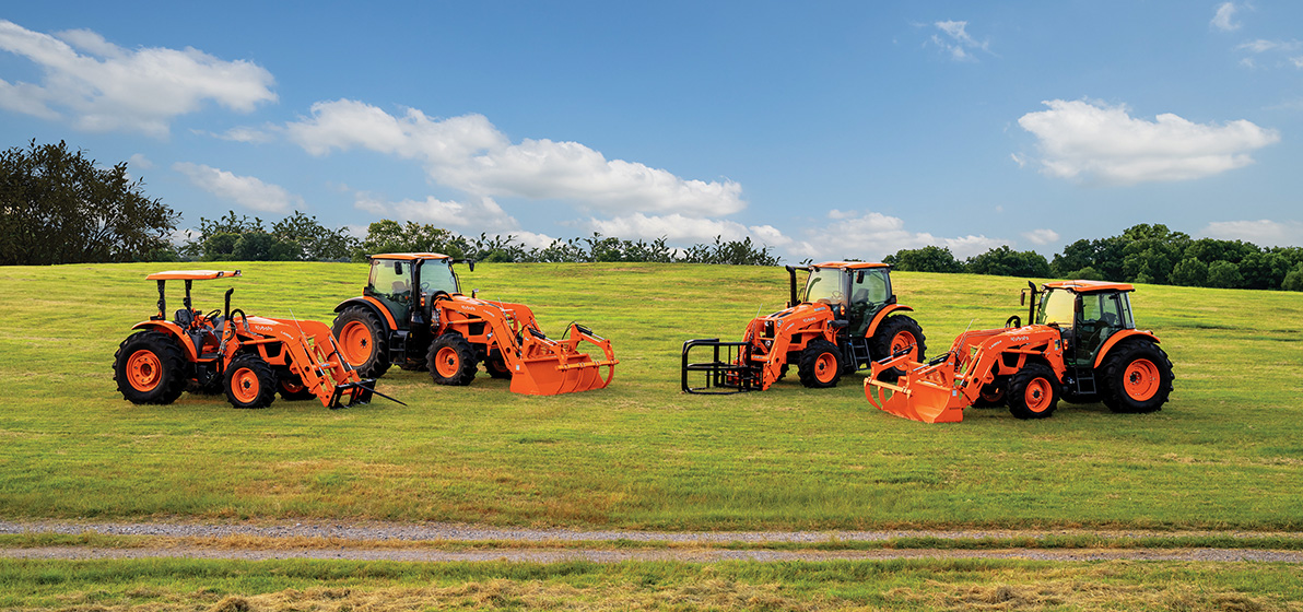 Four Kubota M Series Utility Tractors with various attachments, positioned next to each other near a dirt path.
