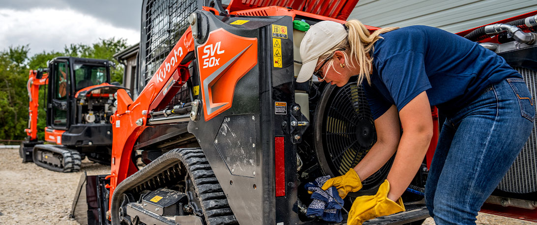 Woman with long hair in a ponytail checking the oil on a Kubota SVL50x track loader.
