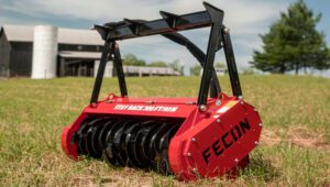 Bullhog Standard Flow Head Attachment isolated in a field with some buildings and trees behind it.