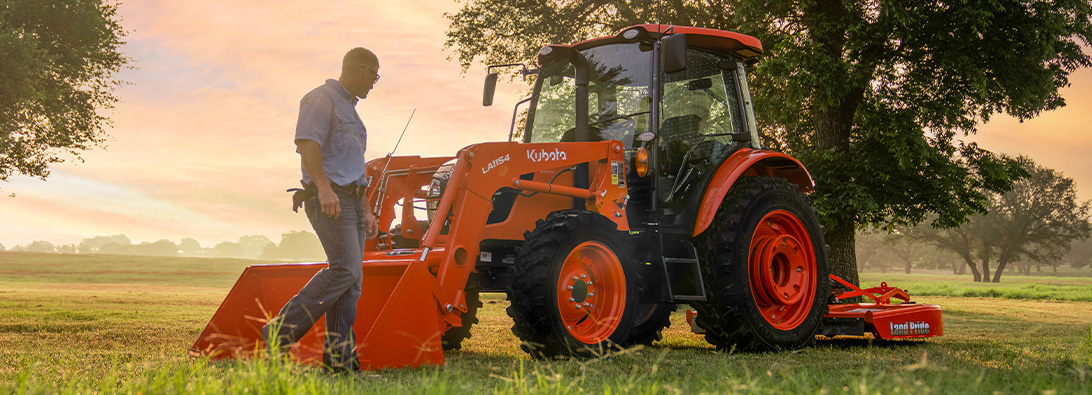 Man walking next to an M Series Kubota tractor in a pasture at sunset.