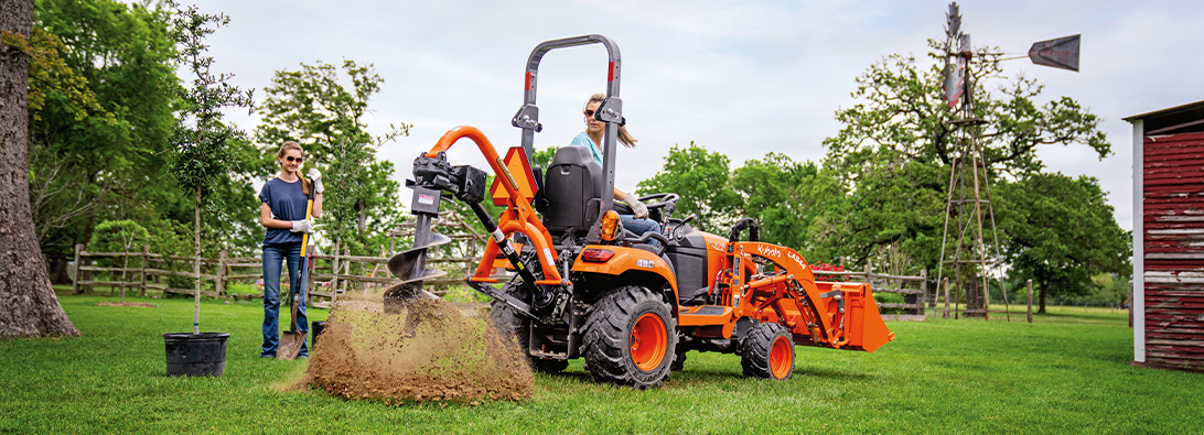 Image of Kubota tractor in a field with a Land Pride auger attachment on the back.