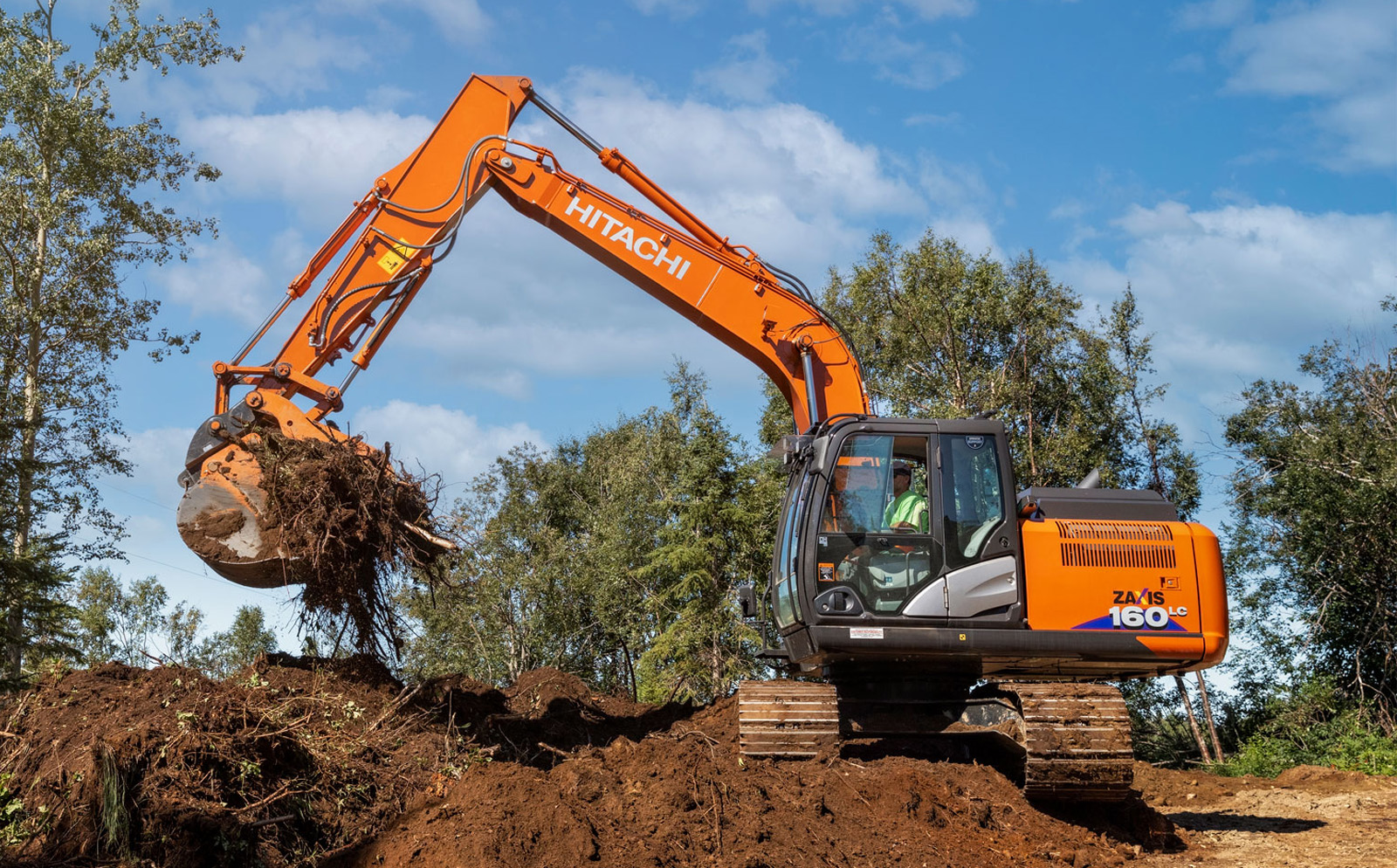 Hitachi excavator at a construction site surrounded by trees.