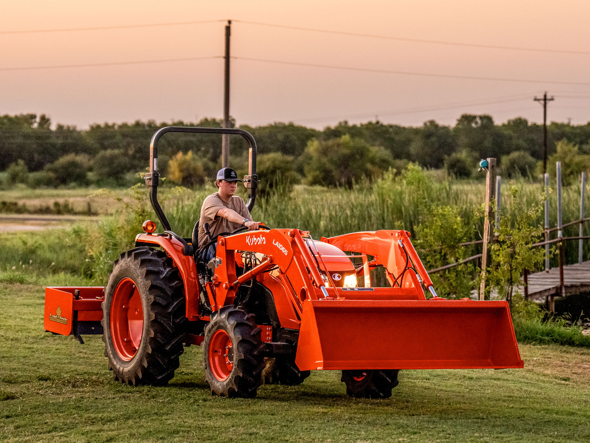 Person driving a Kubota tractor on a warm summer evening.