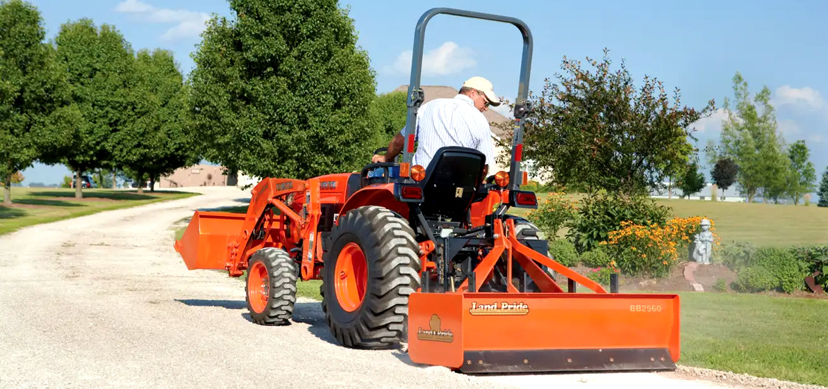Person with a Land Pride attachment driving a Kubota tractor.