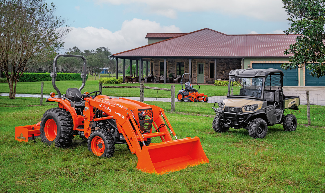 Kubota tractor and RTV on a large residential plot of land in front of a house on a clear day.