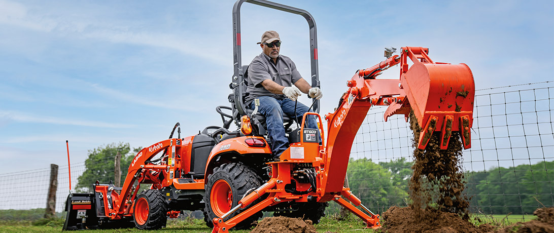 Man in a pasture using a BX23S tractor with digging attachments.