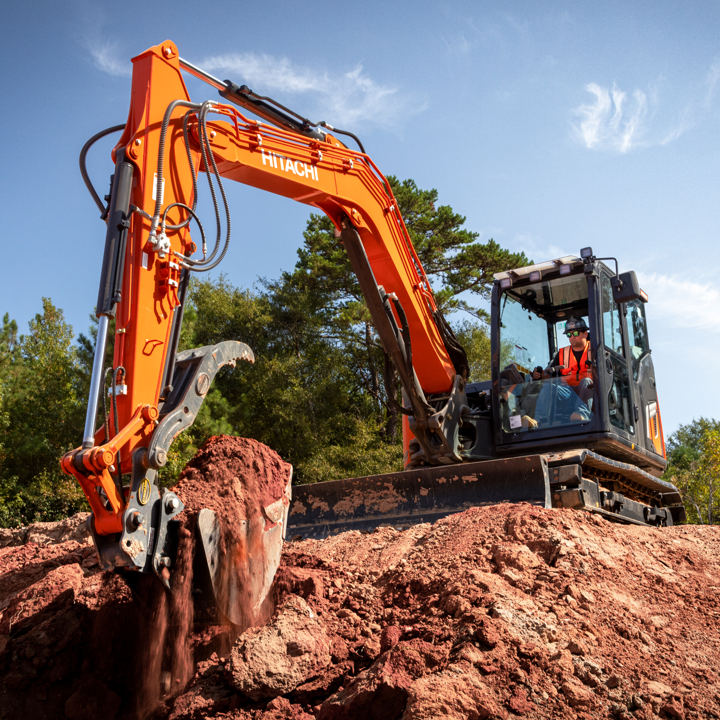Person using a Hitachi ZX85 series compact excavator to clear a construction site on a sunny day.