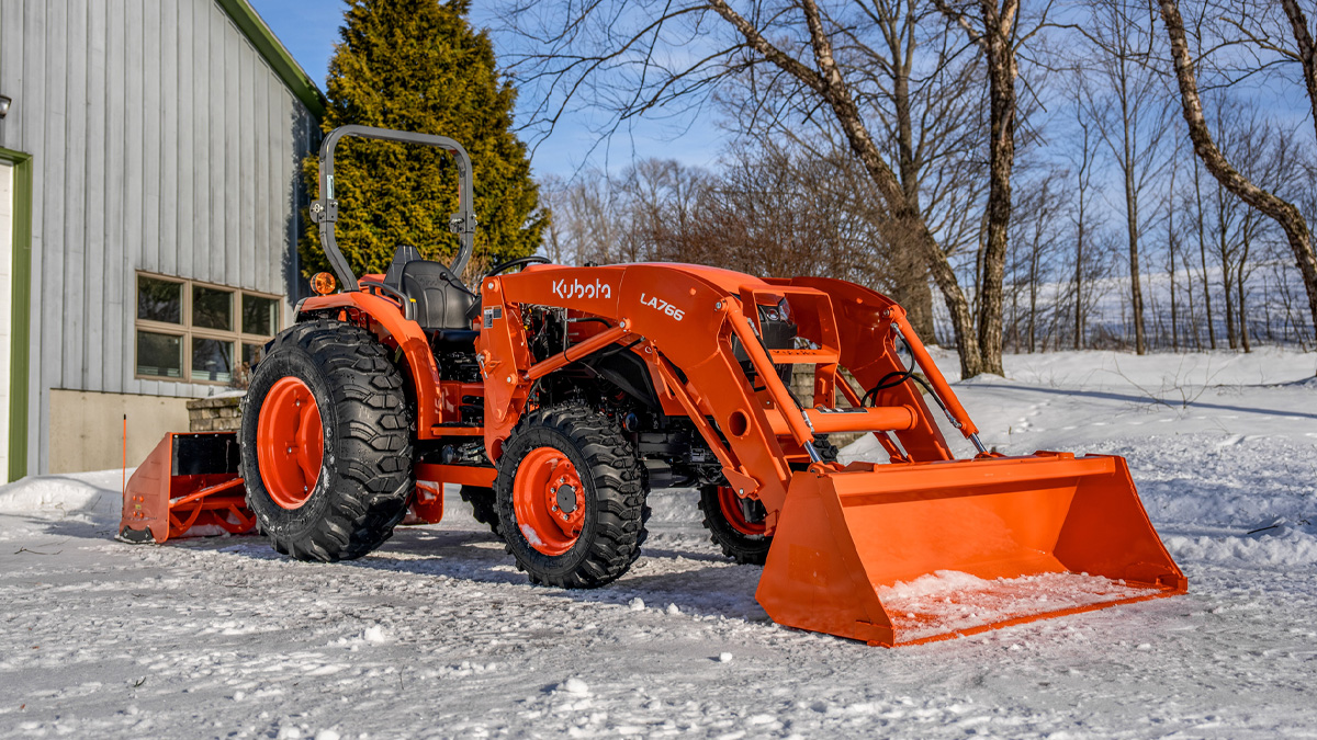 Tractor in a snowy field in front of a Christmas tree.