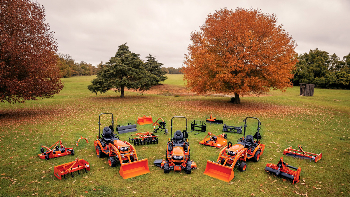 Three Kubota tractors in a field with fall foliage.