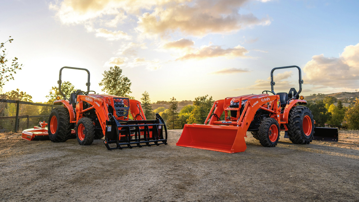 Two Kubota tractors at sunset on gravel.