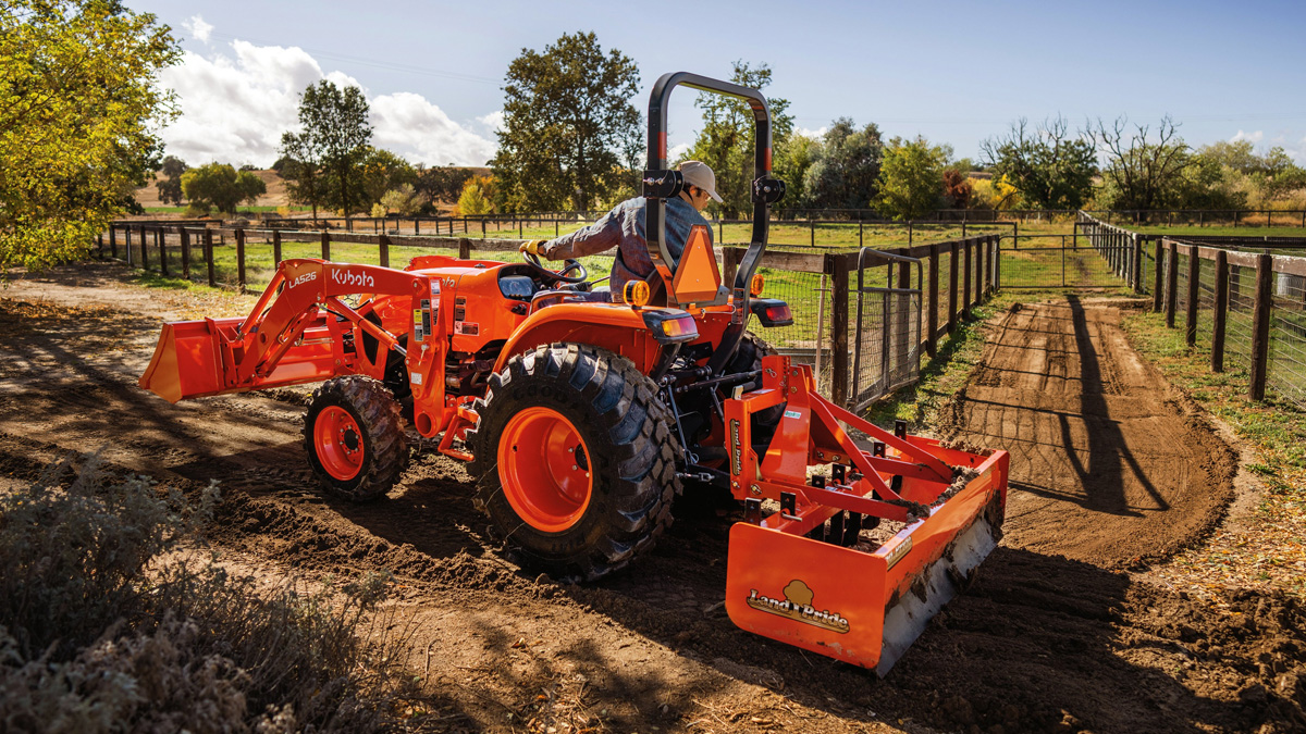 Person driving a Kubota tractor with a Land Pride attachment.