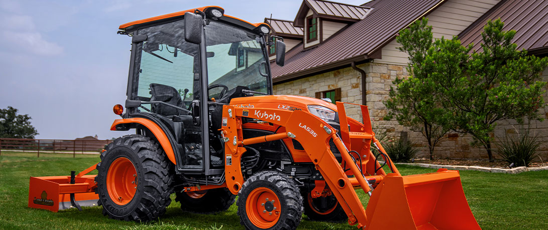 Kubota LX2620 tractor with front-mounted excavator and Land Pride attachment in a residential area.