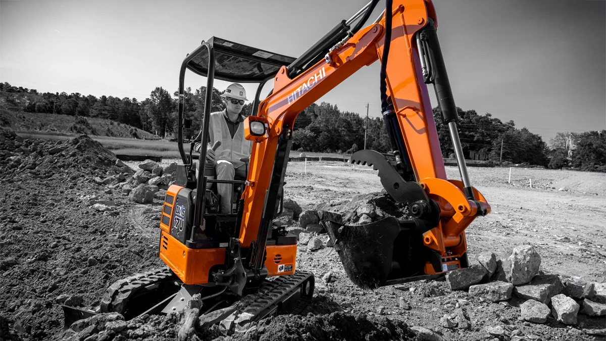 Man using a subcompact Hitachi excavator on a job site.