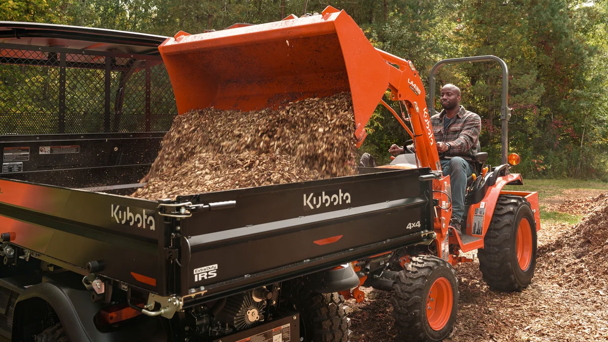 Man in a Kubota tractor dumping rocks into a Kubota RTV.
