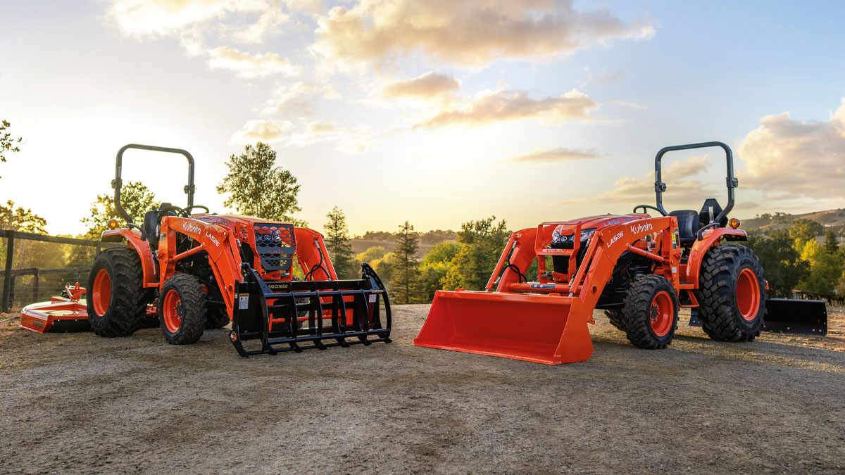 Two Kubota tractors on a gravel road at sunset.