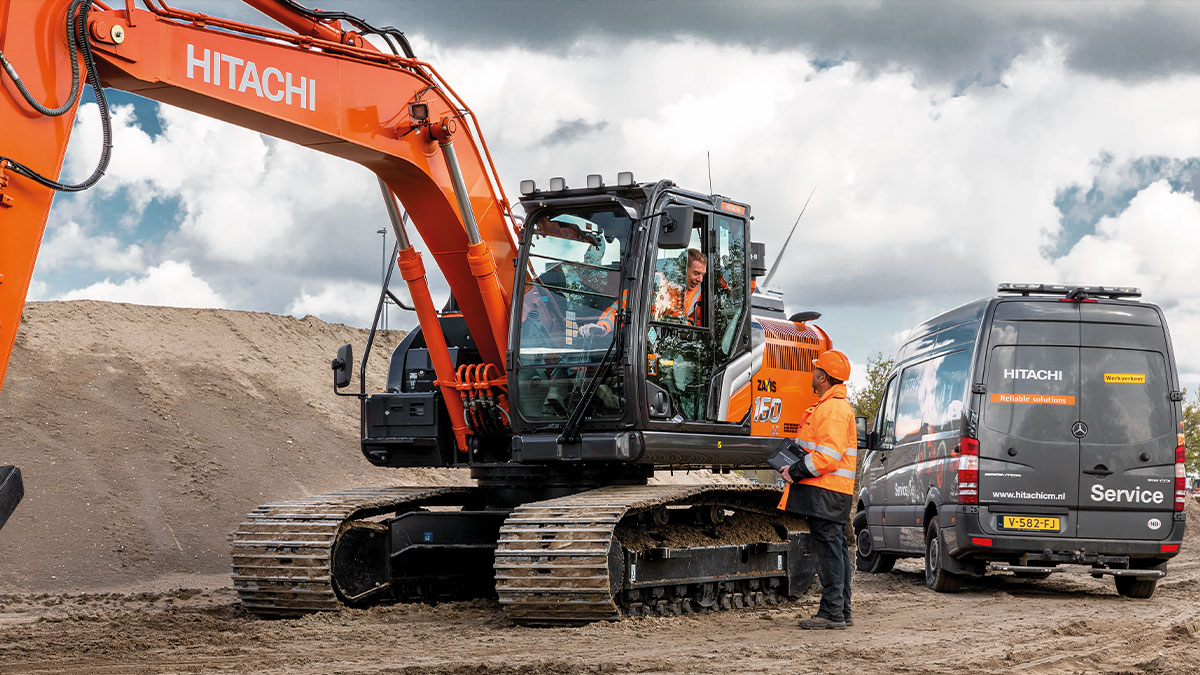 Hitachi excavator on a jobsite with workers standing in front of it.