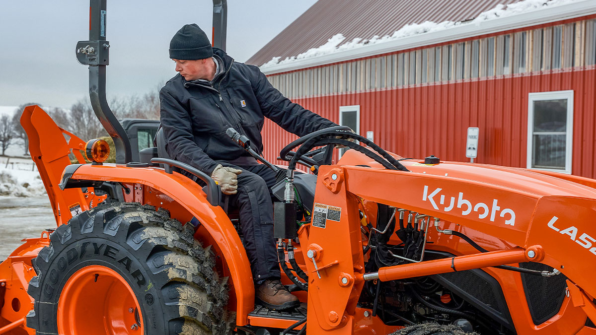 Person in a heavy coat in a winter landscape backing up their Kubota tractor.