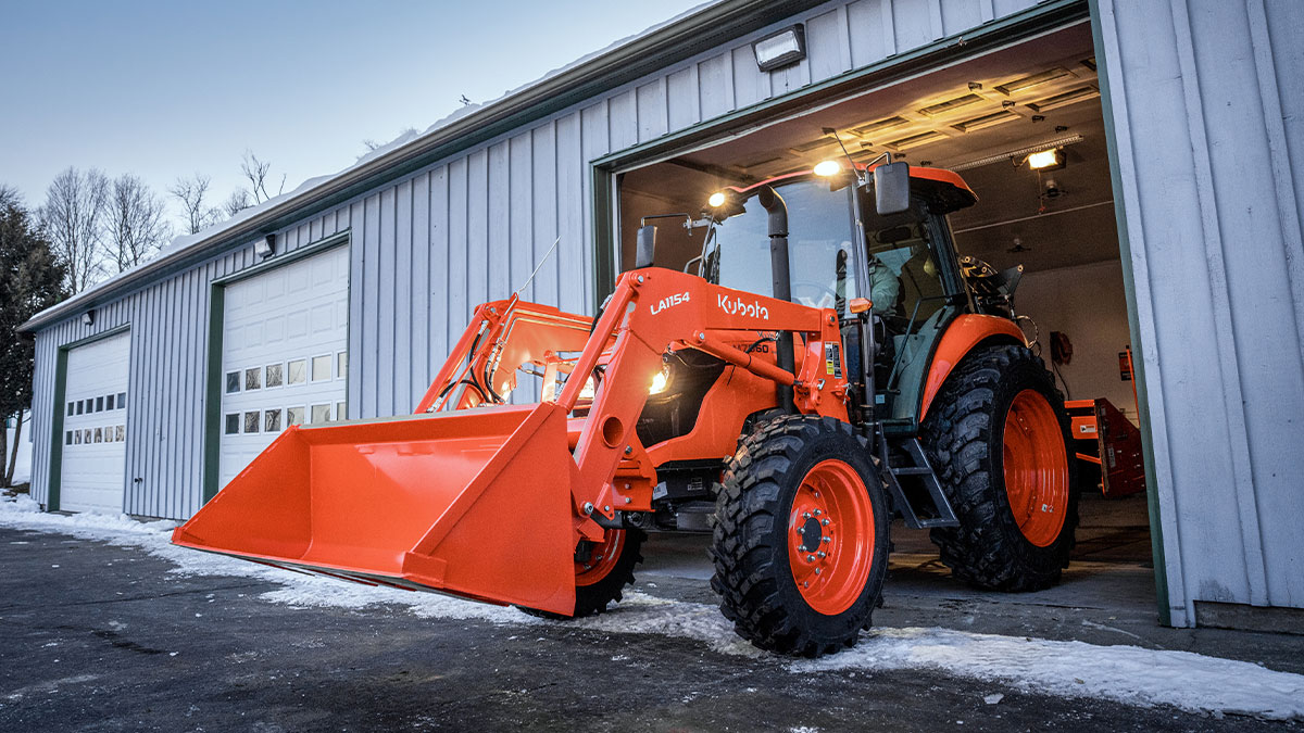 Person driving a Kubota tractor onto a jobsite, exiting a garage.